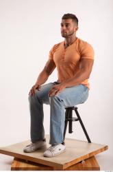 Sitting pose orange thsirt light blue jeans of bodybuilder Harold